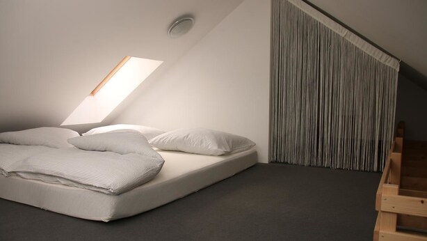 Un dormitorio pequeño y moderno con techo inclinado, una cama individual, tragaluz y un banco de madera.