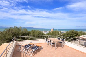 A terrace with a table and chairs, overlooking a coastal view with trees and a distant tower. - House special for families and friends to 100 mt. of the sea. (Colonia de Sant Pere)