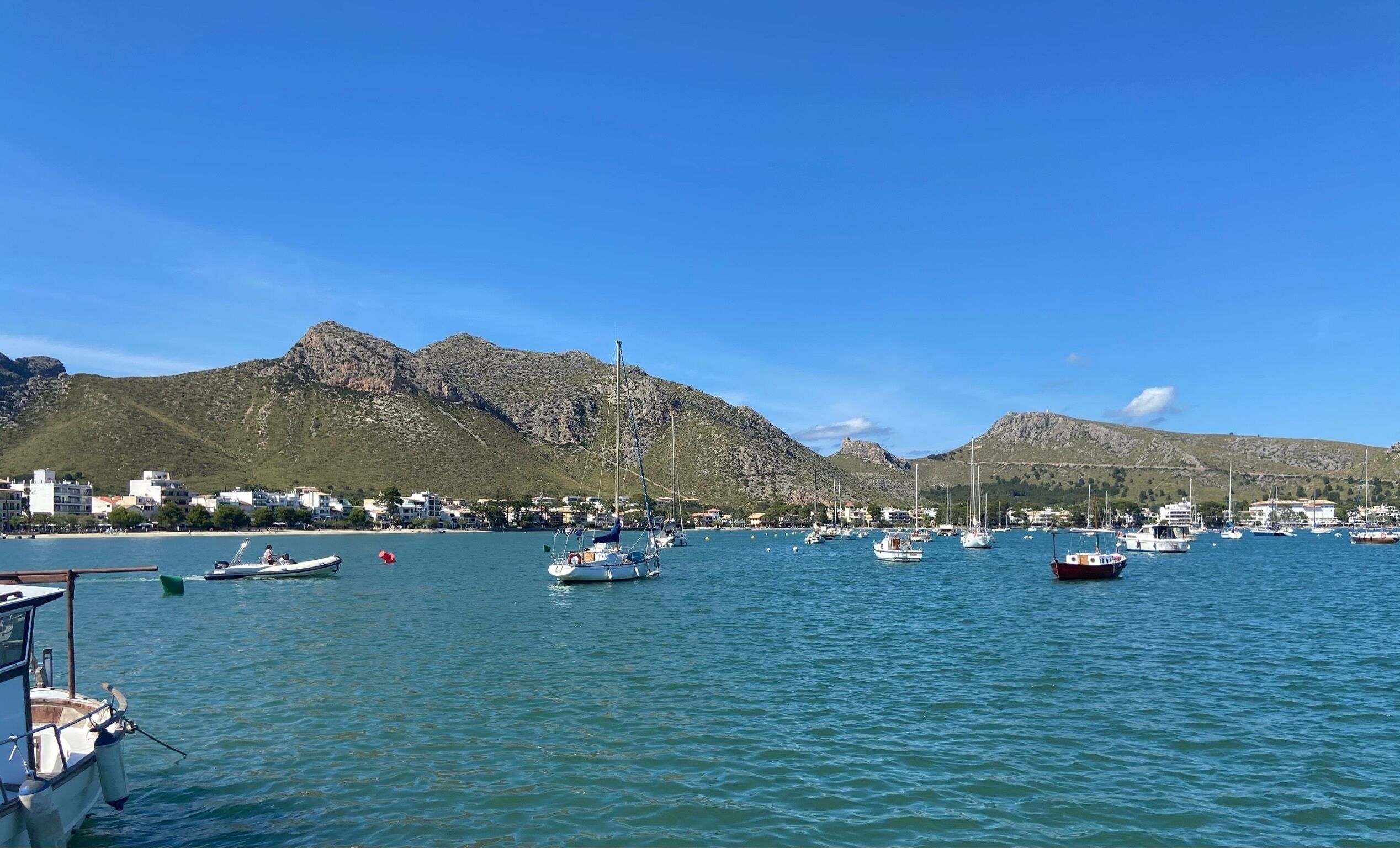 Un puerto deportivo con barcos amarrados, montañas al fondo y edificios a lo largo de la costa.