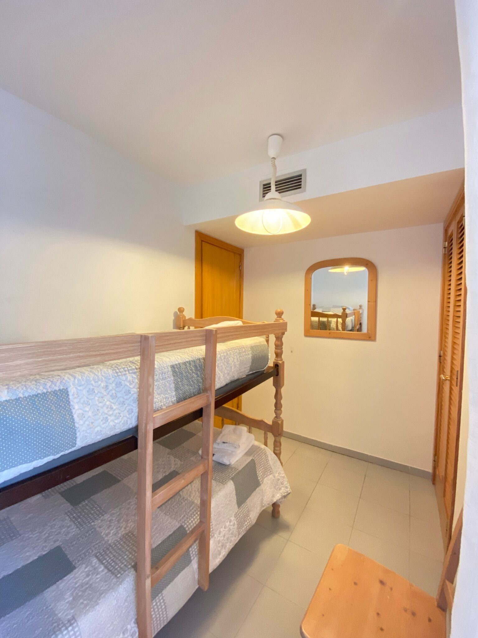 A small, compact room with a bunk bed, a wooden table, a mirror, and a door.