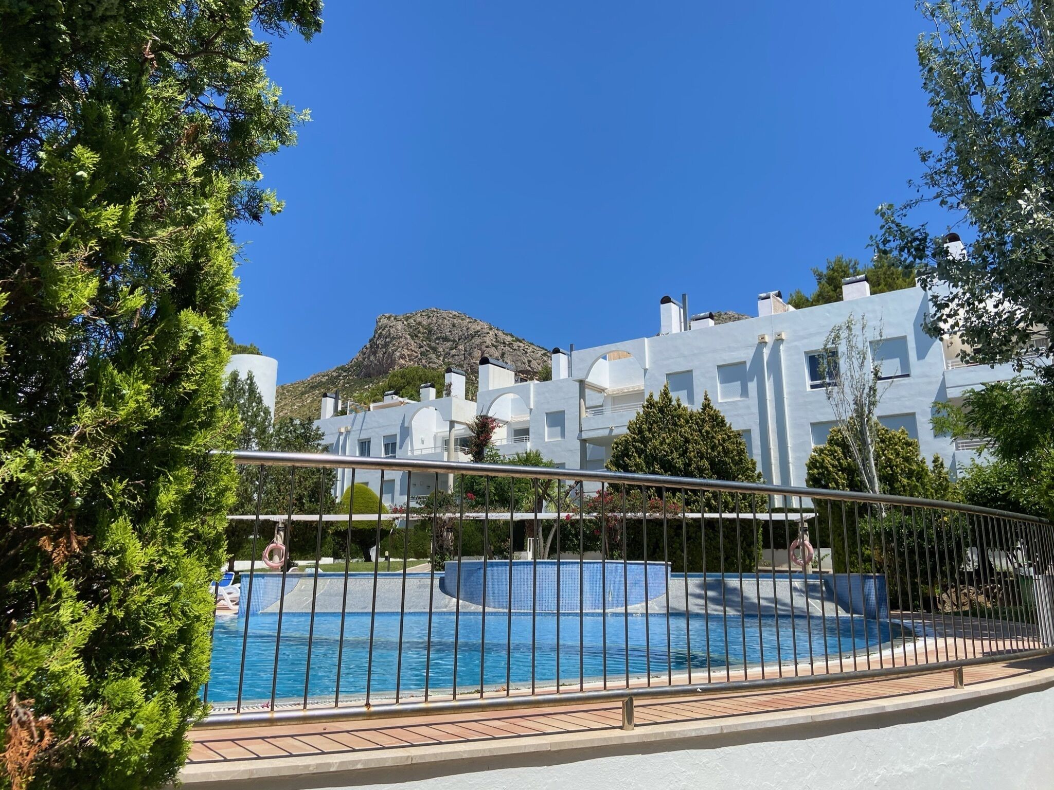 Ein modernes Gebäude mit Poolbereich, umgeben von Grünflächen und blauem Himmel.