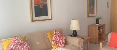 Una sala de estar con un sofá, una mesa de centro, una lámpara y un mueble bajo.