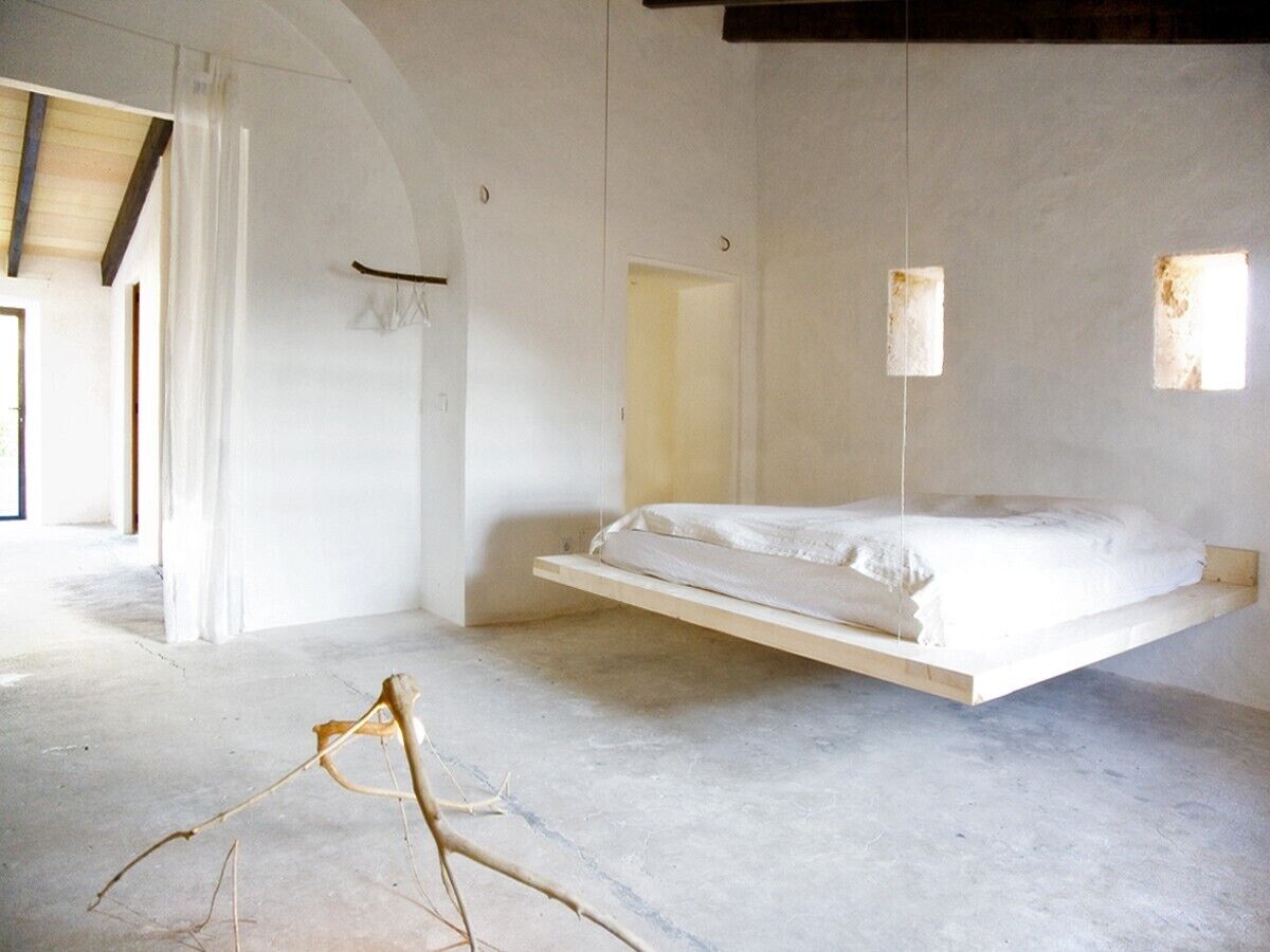 A minimalist room with a suspended bed, concrete floor, and an arched doorway.