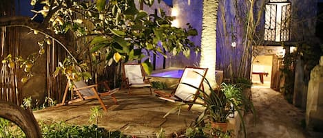 Un espace extérieur aménagé avec des chaises et une table en bois, entouré de plantes en pot et d’une petite piscine.