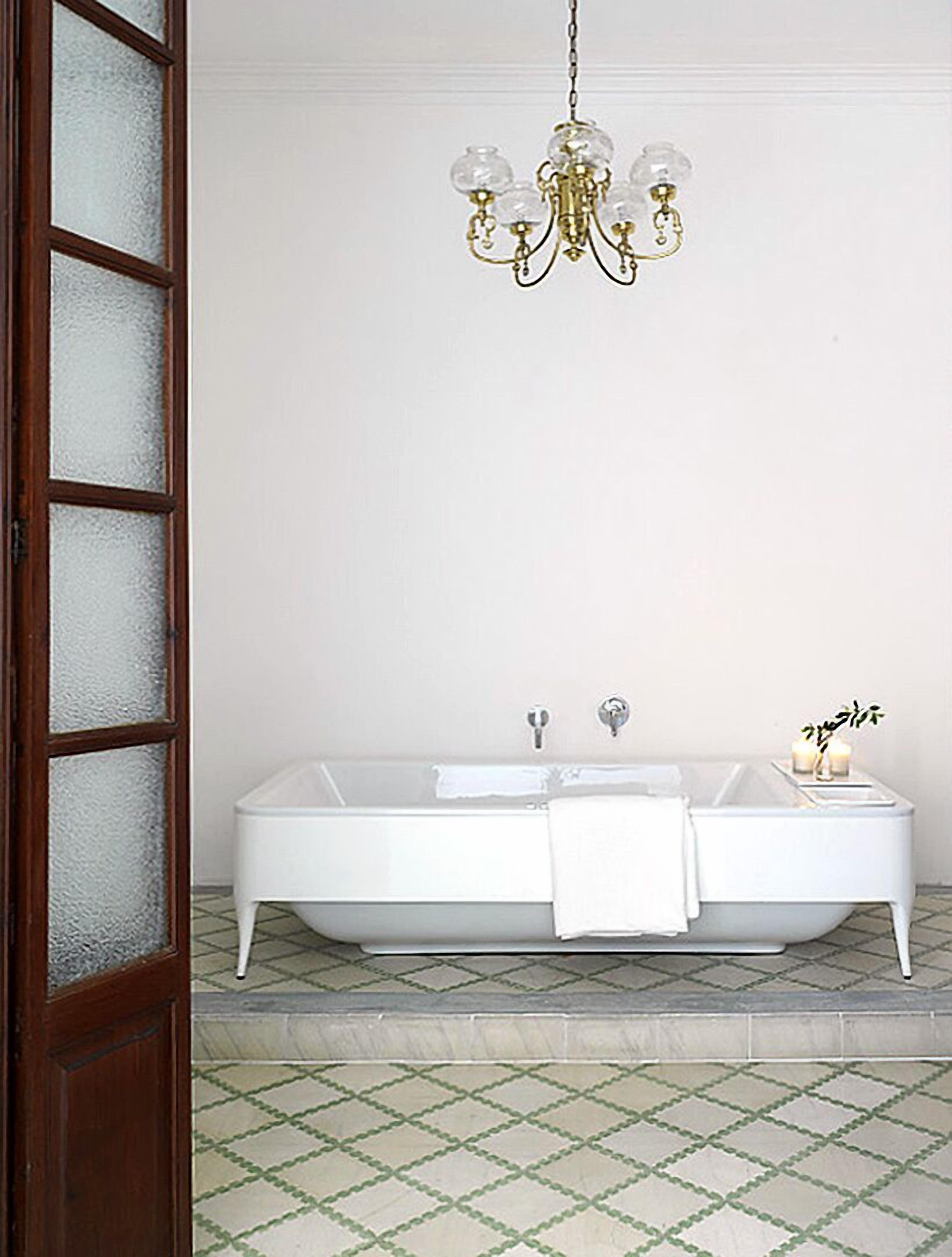 A bathroom with a freestanding bathtub, a chandelier, and a frosted glass door.