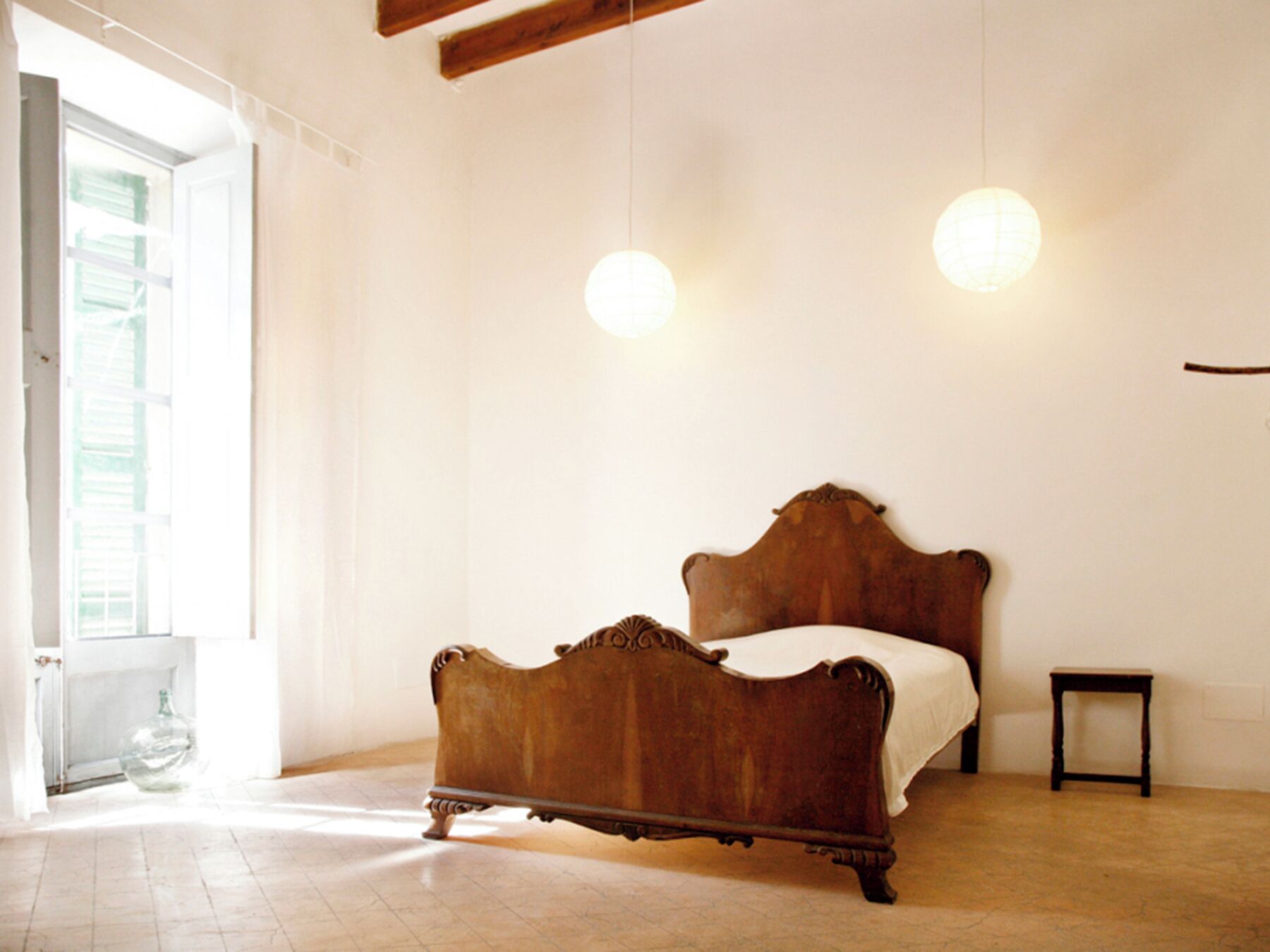 A bedroom with a wooden bed, a small bedside table, and a hanging light fixture.