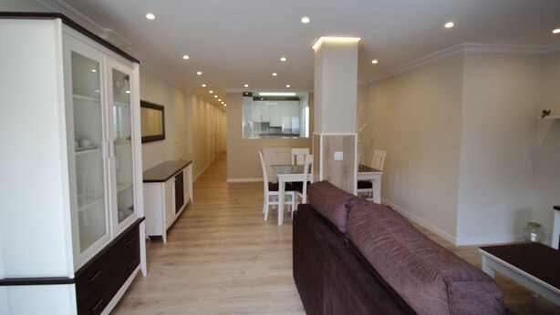 A modern kitchen with white cabinets and a dining area with a brown sofa.