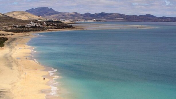A coastal beach with clear turquoise waters, a sandy shore, and distant mountains. - AMAZING SEA VIEW LUXURY APARTMENT- WITH SUN DRENCHED SPACIOUS TERRACE/FREE WiFi (Gran Tarajal, Tuineje)