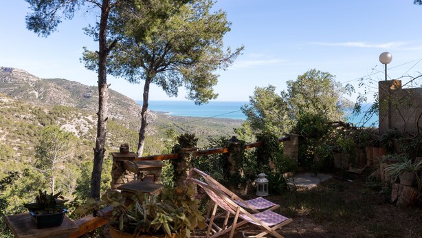 A patio with a view of the sea, surrounded by potted plants and a wooden fence.