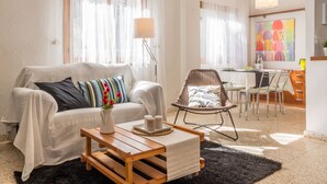 A modern living room with a sofa, a coffee table, a dining area with chairs, and a painting on the wall.