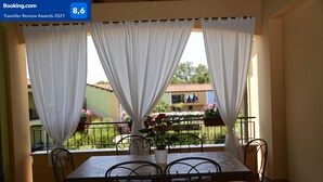 A balcony with a table and chairs, white curtains, and a view of buildings and greenery. - AFRODITE-Elegant villa overlooking pool. (Policoro)