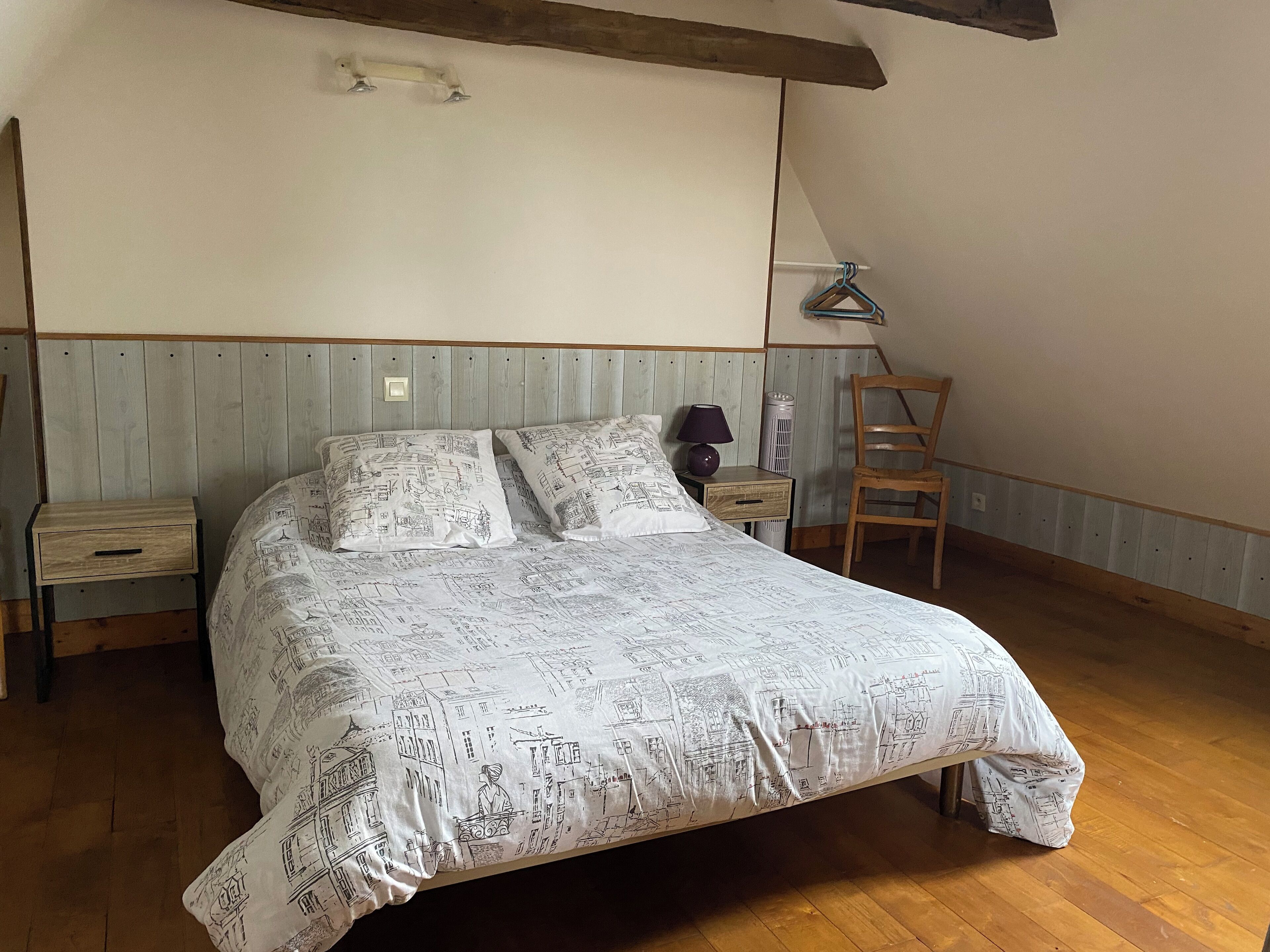 A bedroom with a bed, a nightstand, a chair, and a hanging lamp.