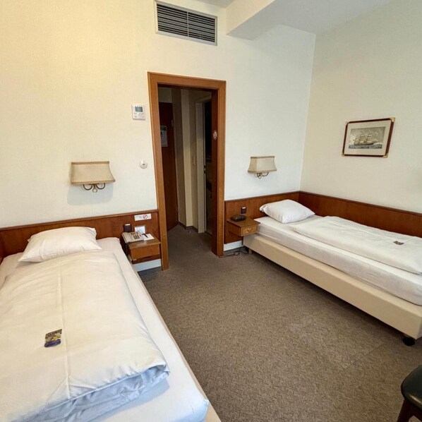 Quarto de hotel com duas camas, uma mesa de cabeceira com telefone, abajur e um quadro na parede.