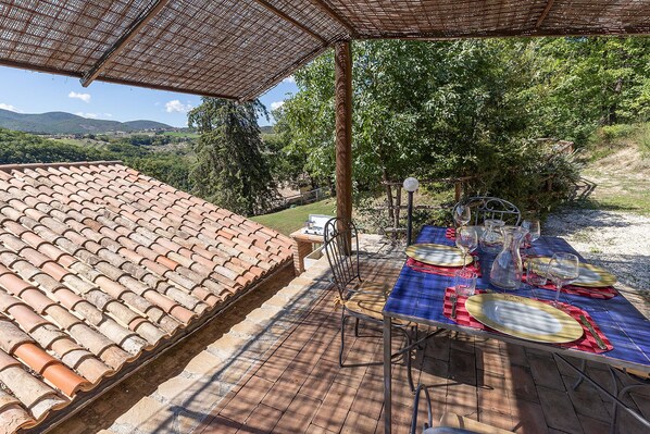 An outdoor patio with a tiled roof, a table set for dining, and a view of the countryside. - Villa Carina is a cozy cottage w/pool the ideal locaton for relaxation in Umbria (Collelungo di Baschi)