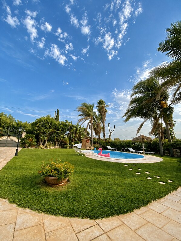 Un pati d'hivern amb piscina, palmeres i un jardí ben cuidat.