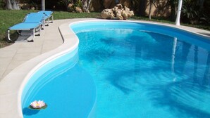 A swimming pool with a curved edge, a lounge area with benches, and a rock formation in the background. - VILLA ORCHIDEA, PRIVATE POOL SAN LORENZO AND MARZAMEMI A FEW STEPS FROM THE  SEA (san lorenzo)