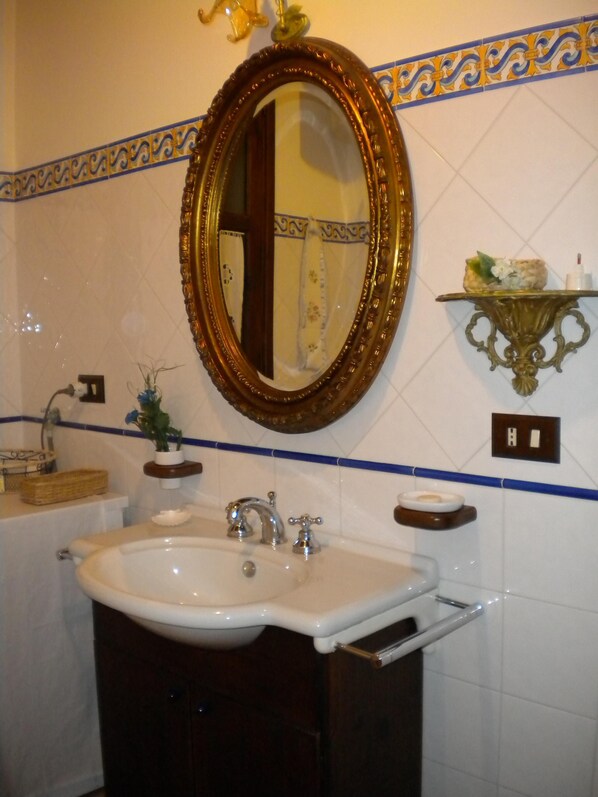 Een badkamer met een wit wastafelmeubel, een spiegel met gouden lijst en decoratieve blauwe en gele tegels.