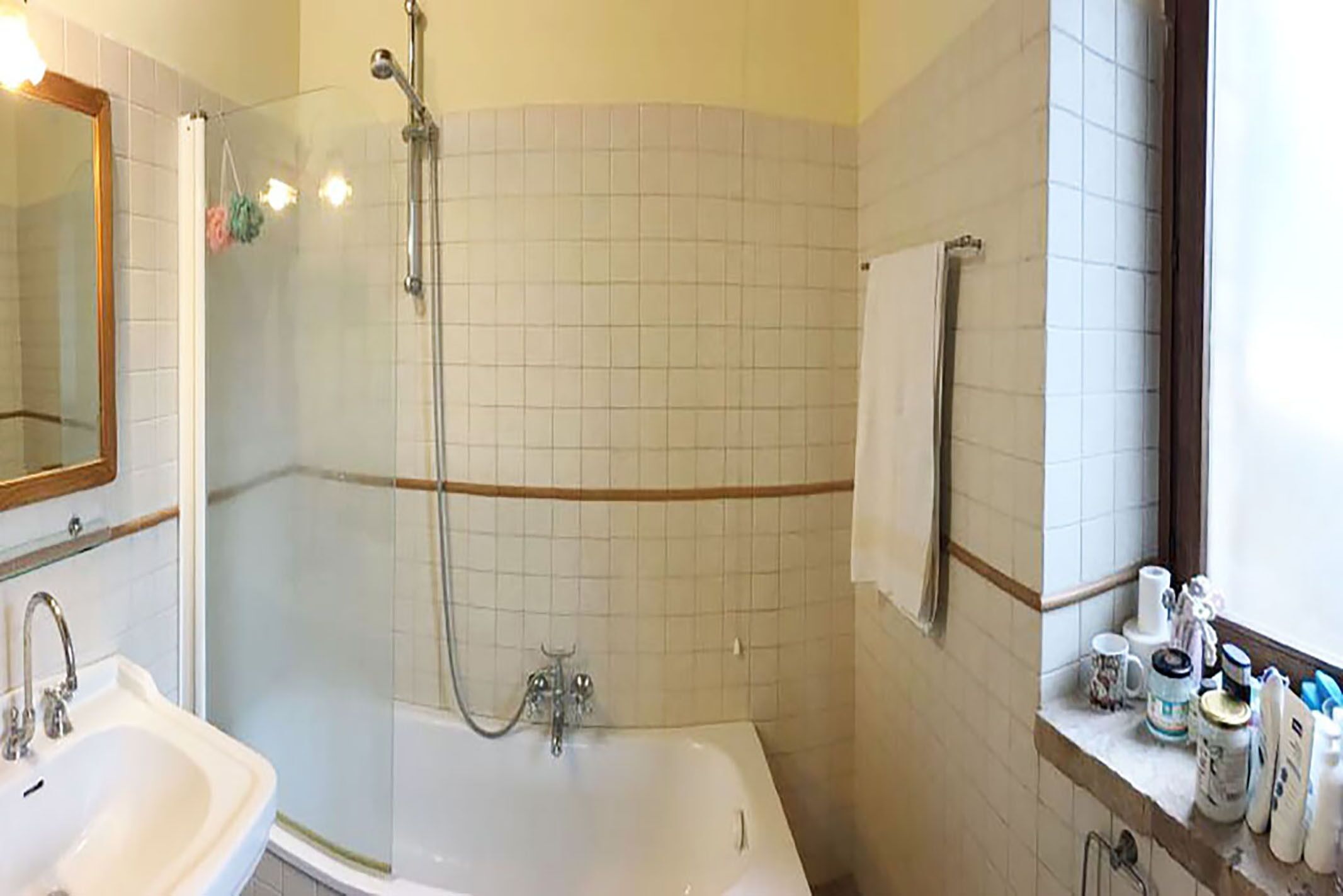 Un baño con ducha, lavabo y bañera. Hay un espejo sobre el lavabo y un perchero encima de la bañera.