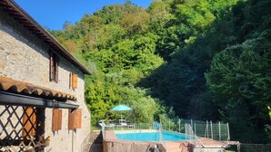 A stone building with a pool, surrounded by lush greenery and a fenced area.
