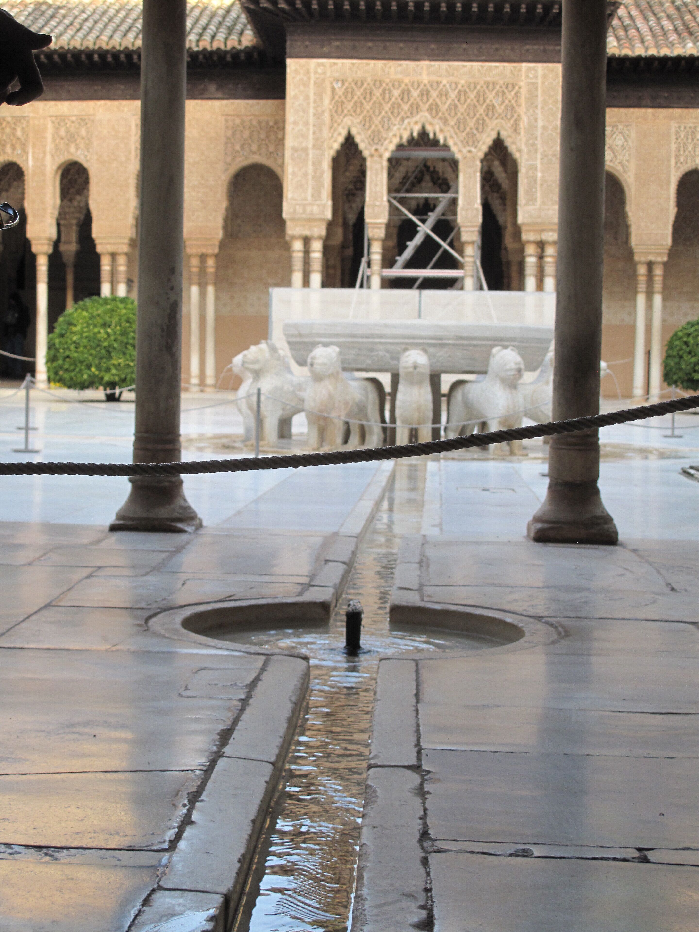 A courtyard with a fountain, stone lions, and a building with arches in the background.
