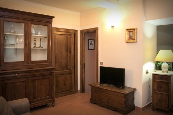 Un salon avec un meuble en bois, un téléviseur posé sur un support en bois, une lampe et un tableau encadré accroché au mur.
