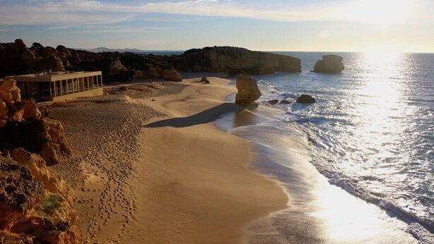 A beach with a building on the left, rocky formations, and the ocean.