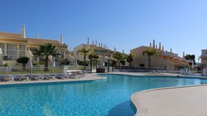 A swimming pool with lounge chairs and umbrellas, surrounded by buildings with tiled roofs and chimneys.