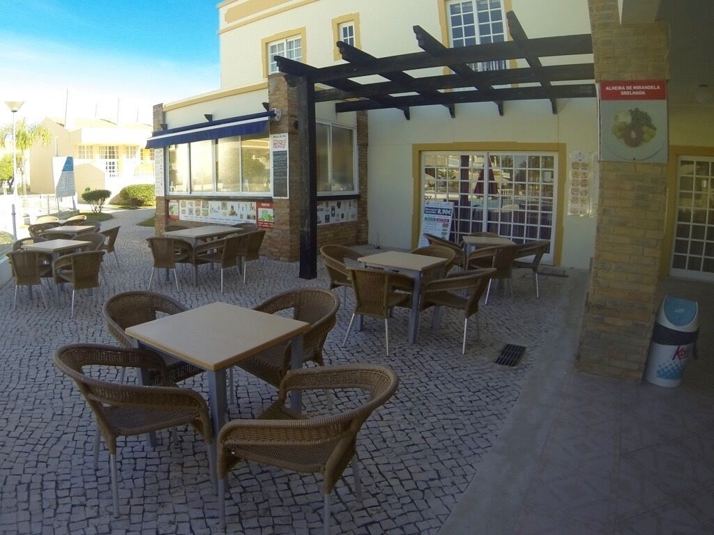 An outdoor cafe area with wicker tables and chairs, a pergola, and a tiled floor.