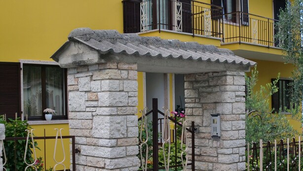 Un edificio amarillo con pilares de piedra, una entrada porticada y un balcón con barandilla de metal.