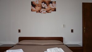 Un dormitorio con cama de madera, dos toallas blancas, una puerta de madera y una obra de arte floral colgada en la pared.