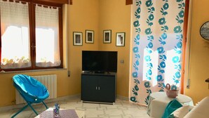 Un soggiorno con una televisione, una poltrona blu, un divano e un tavolino con una bottiglia.