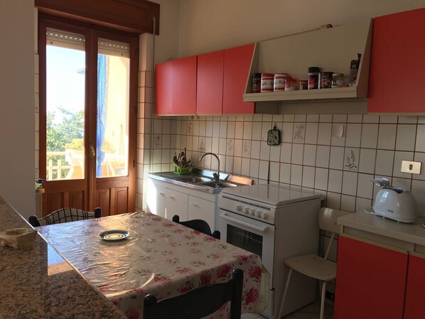 Een keuken met een fornuis, spoelbak en rode kastjes.