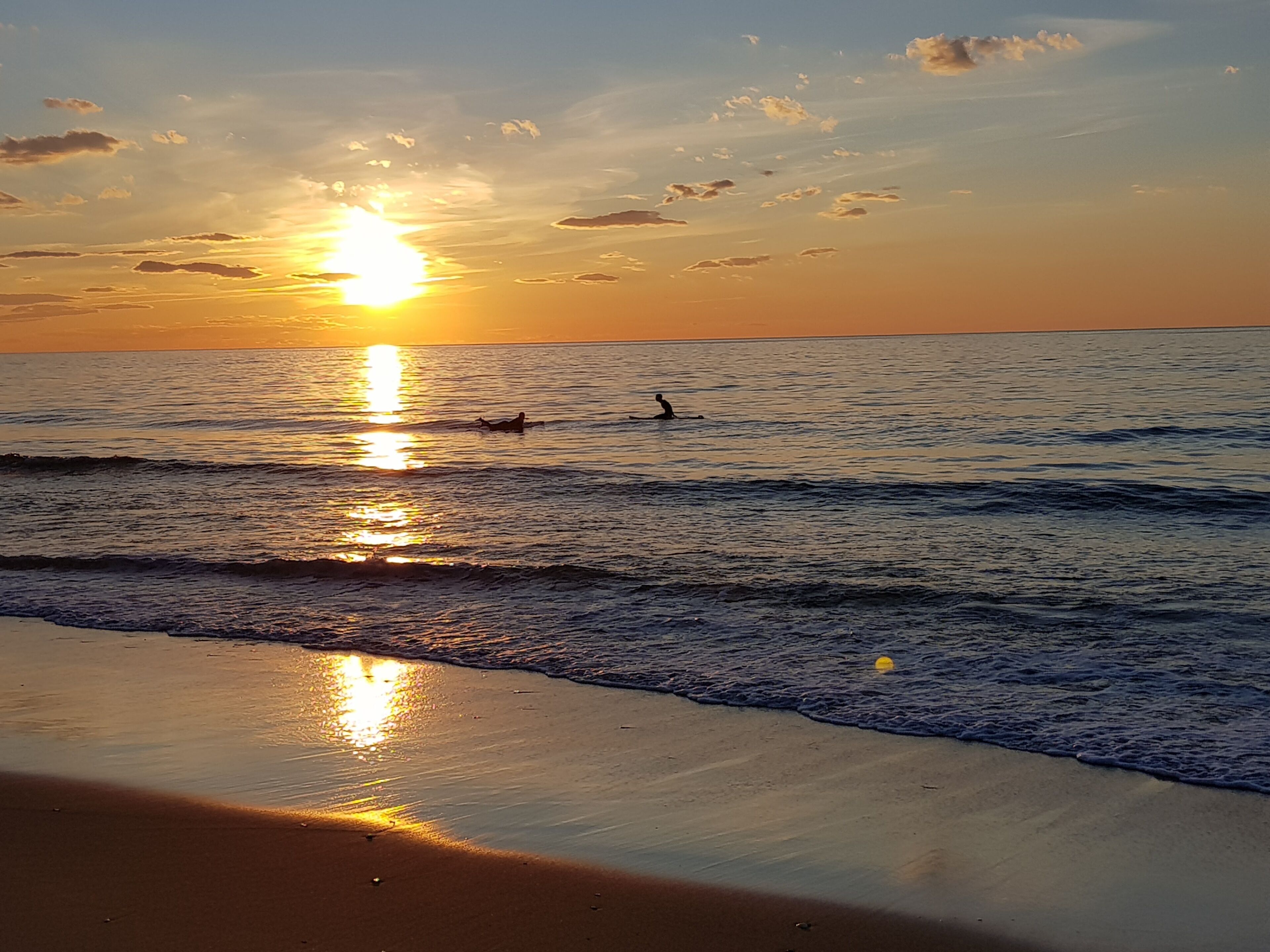 Une plage où le soleil se couche sur l’océan, et où les vagues viennent doucement lécher le rivage.