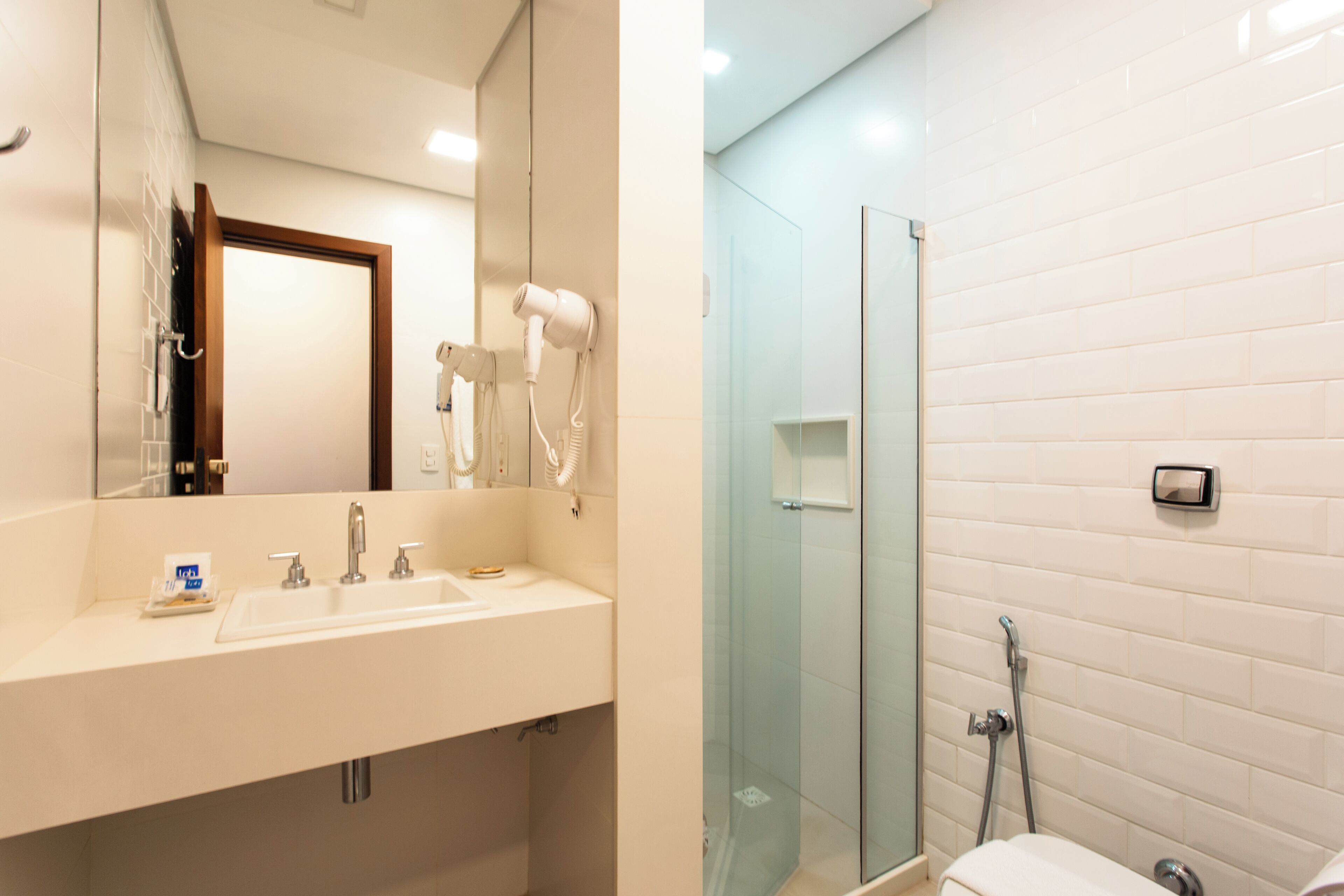 Un baño con lavamanos blanco, espejo, secador de pelo y cabina de ducha de vidrio.