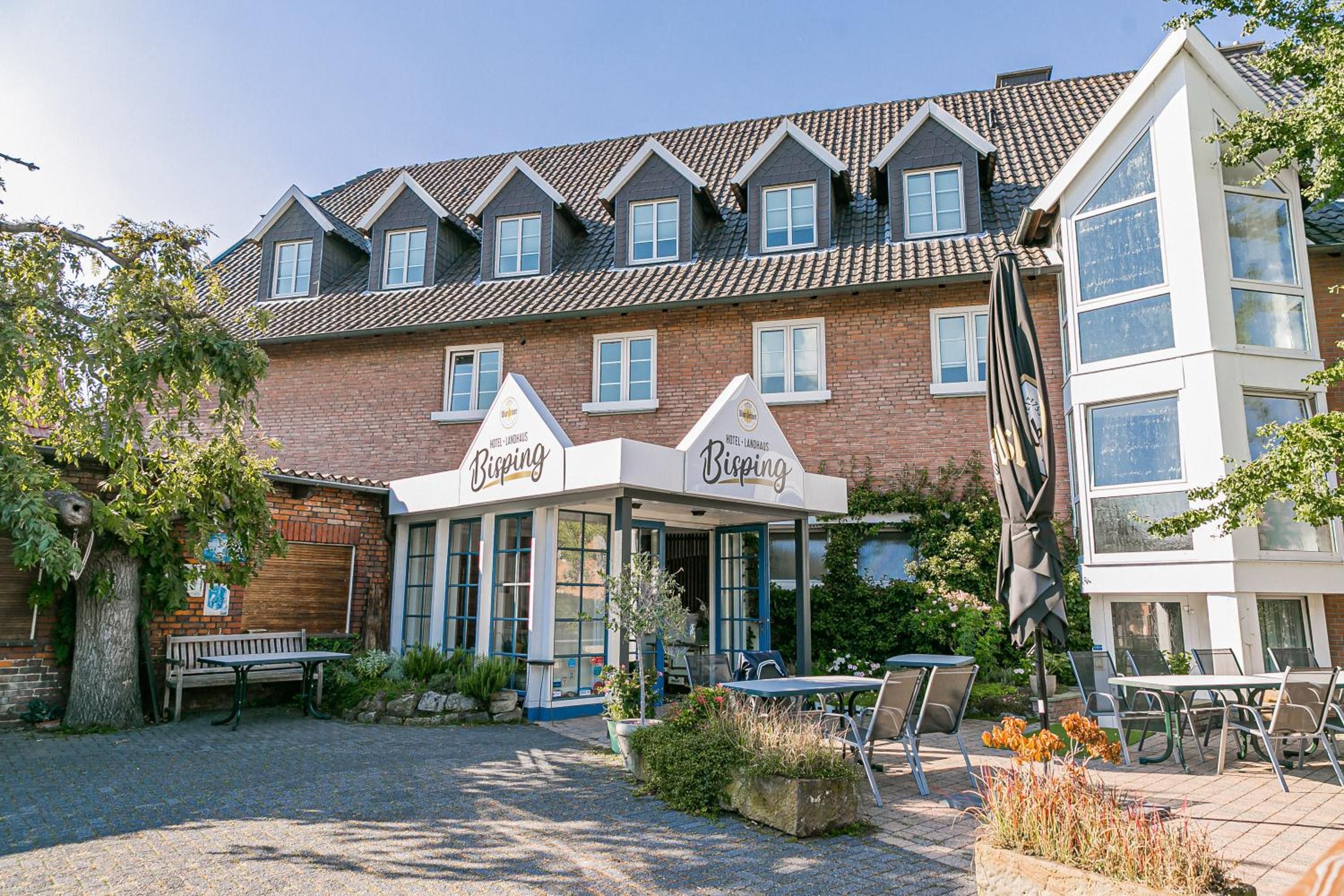 A hotel with a traditional brick facade, multiple windows, and a covered outdoor seating area with tables and chairs.