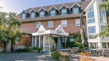 A hotel with a traditional brick facade, multiple windows, and a covered outdoor seating area with tables and chairs.