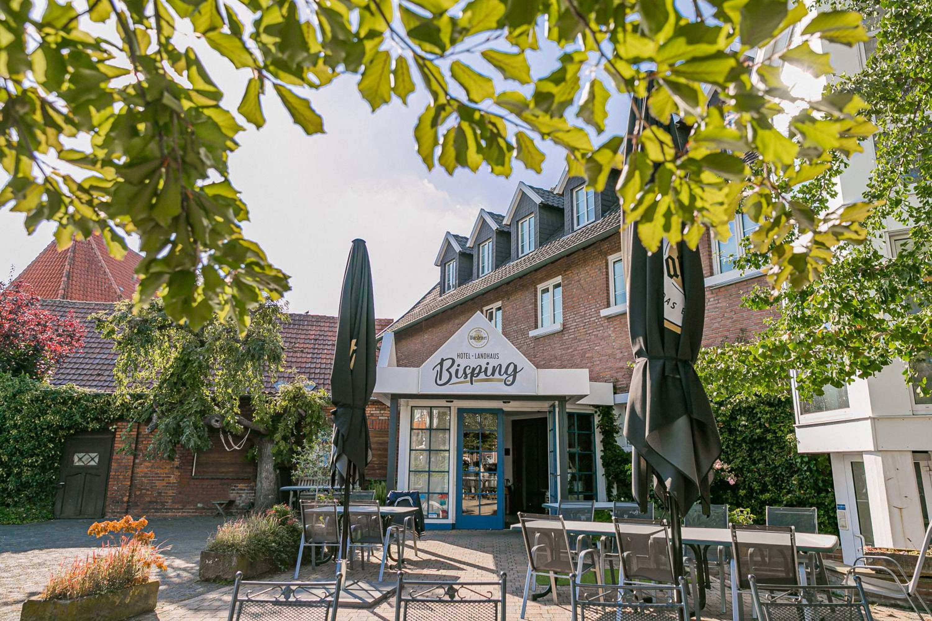 A hotel named 'Hotel Landhaus Bisping' with outdoor seating and a brick facade.