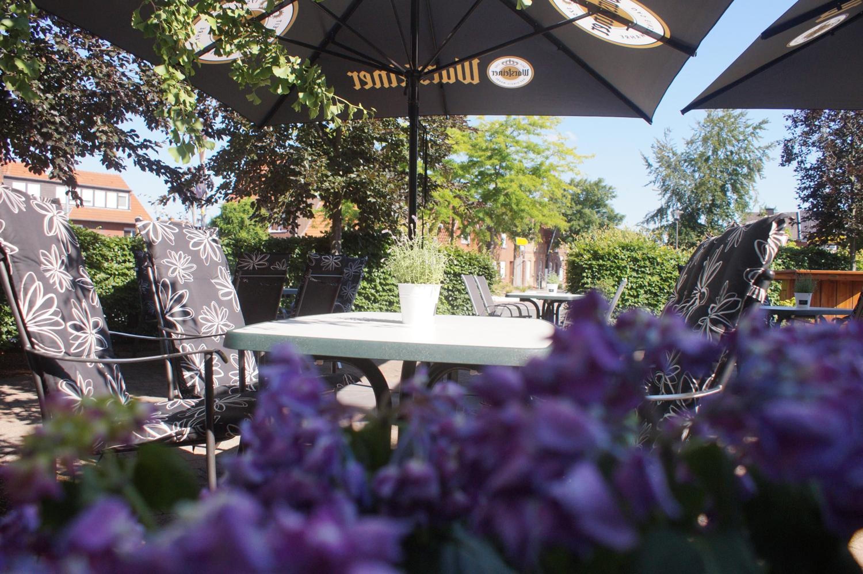 An outdoor seating area with tables and chairs, surrounded by greenery and a clear sky.
