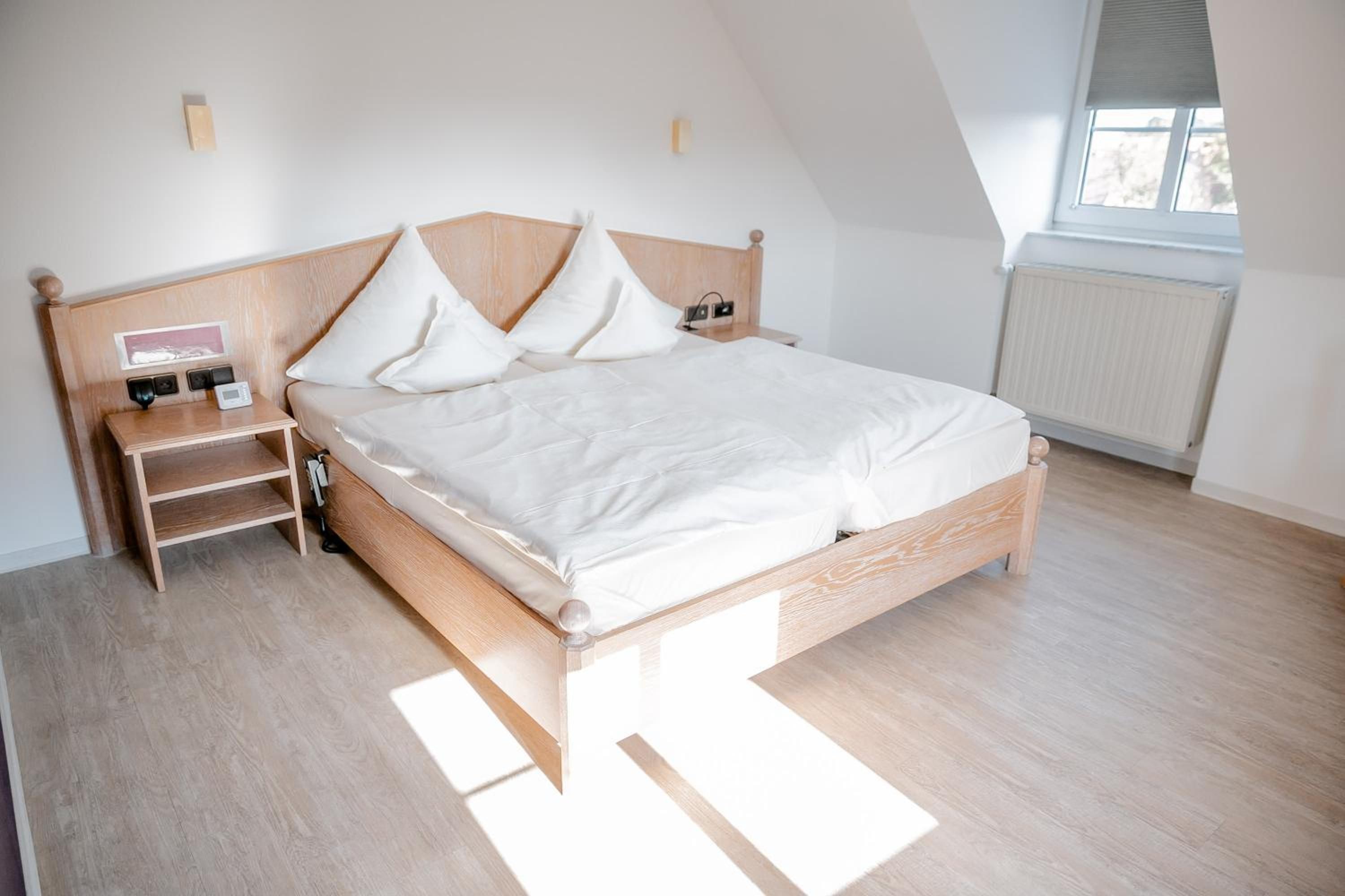 A bedroom with a wooden bed, white bedding, a nightstand with a lamp, and a window with blinds.