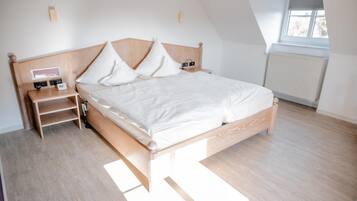 A bedroom with a wooden bed, white bedding, a nightstand with a lamp, and a window with blinds.