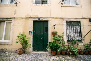 A building with a green door, multiple potted plants, and a window with a metal grill.