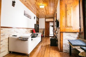 A cozy room with a wooden ceiling, a white sofa with a red pillow, a bench, and a stone wall.