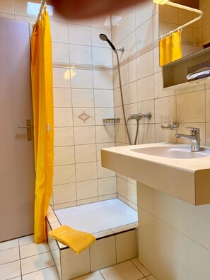 A bathroom with a shower, a sink, and a yellow towel on the floor. - Hotel Zum Roten Lv Wen (Hildisrieden)