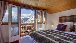 A cozy room with a bed, a window with a mountain view, and a wooden ceiling.