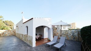 Un patio en la azotea con un muro de piedra, una pequeña zona de comedor y dos sillones de lounge bajo una sombrilla.