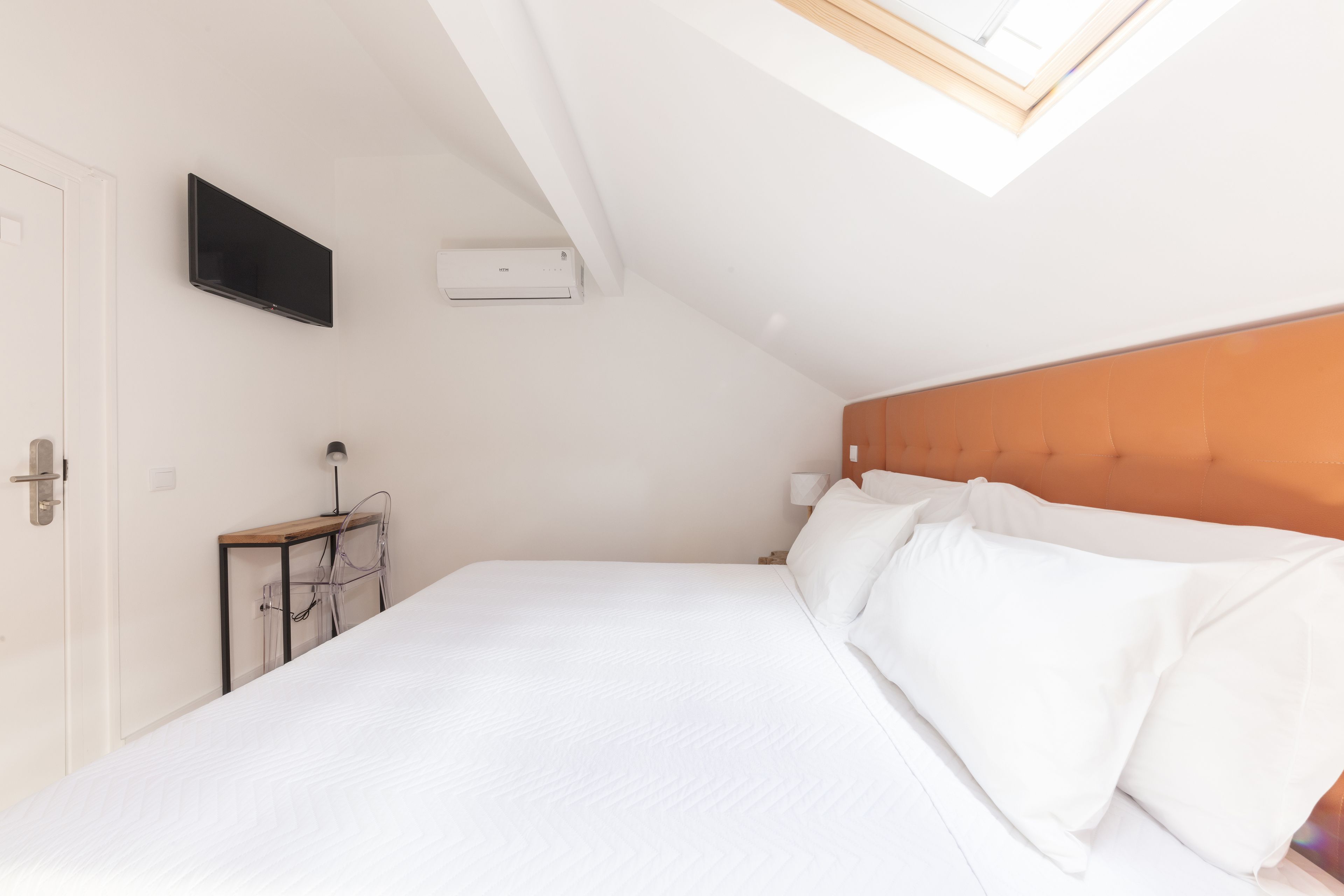 A bedroom with a bed, a TV mounted on the wall, and an air conditioning unit.