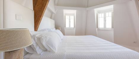 A bedroom with a large bed, wooden beams, and a chandelier.