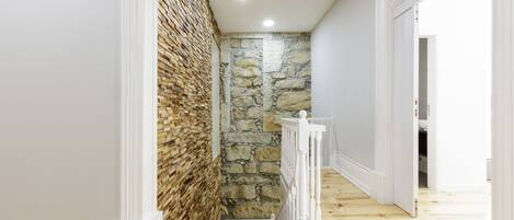 A hallway with a wooden floor, white walls, and a stone wall on one side.