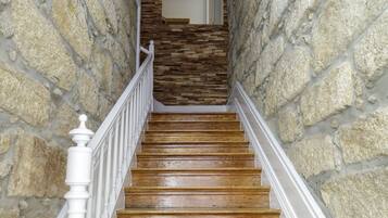 A wooden staircase with white balusters, leading up to a room with a stone wall and a wooden floor.