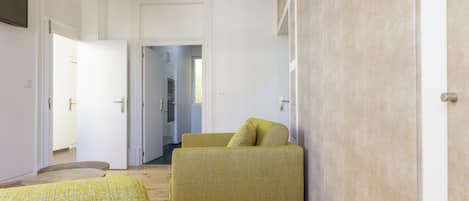 A room with a yellow sofa, a bed with a yellow and white patterned bedspread, and a wooden floor.